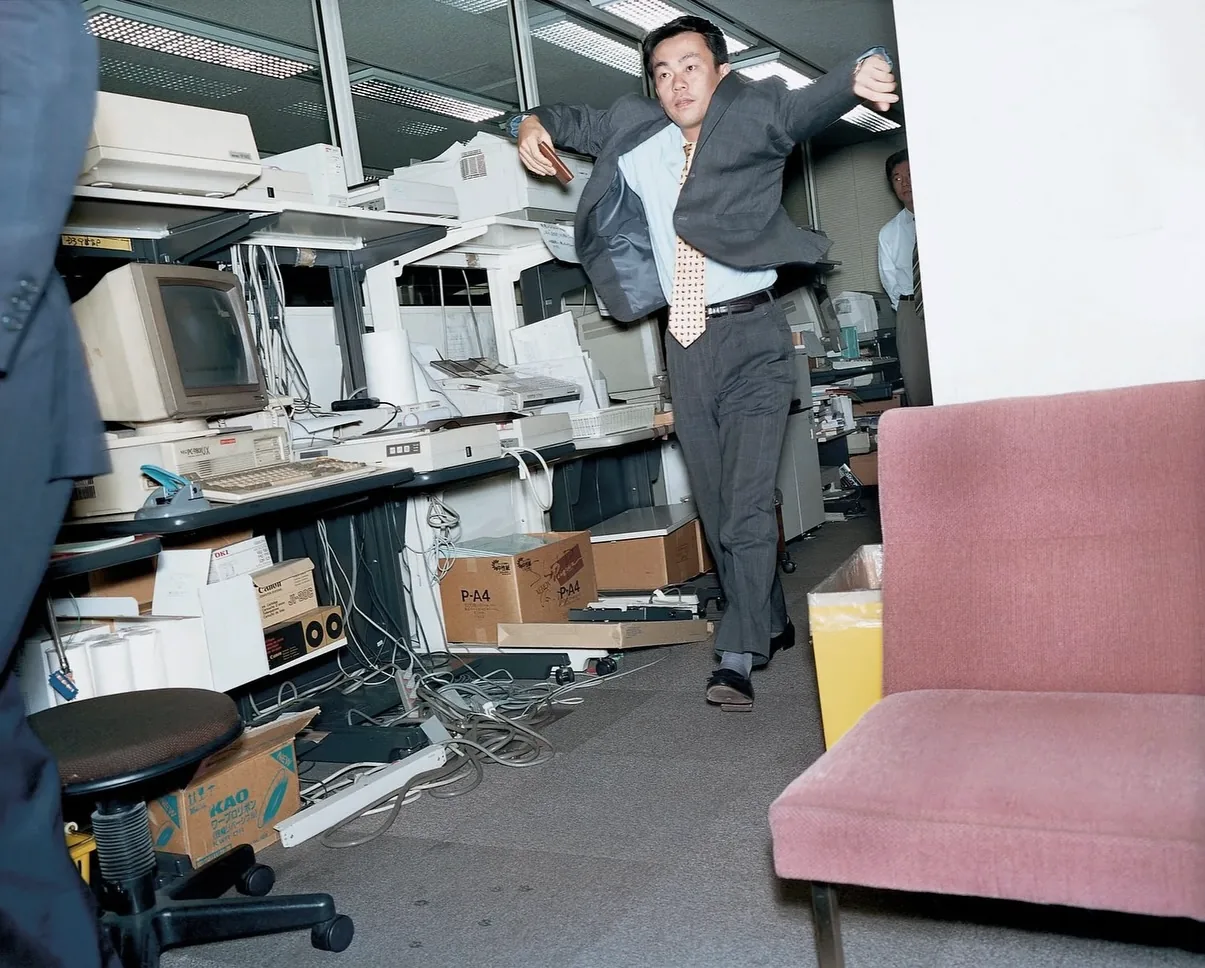 An office worker navigating a cluttered workplace filled with computers, cables, boxes, and paper